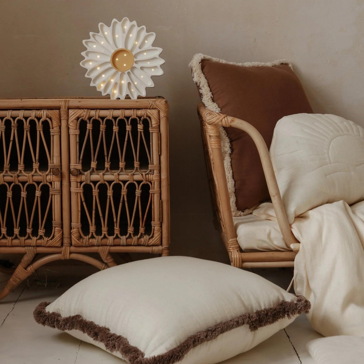 Decorative pillow with brown trim on a wooden floor next to a wicker chair and cabinet.