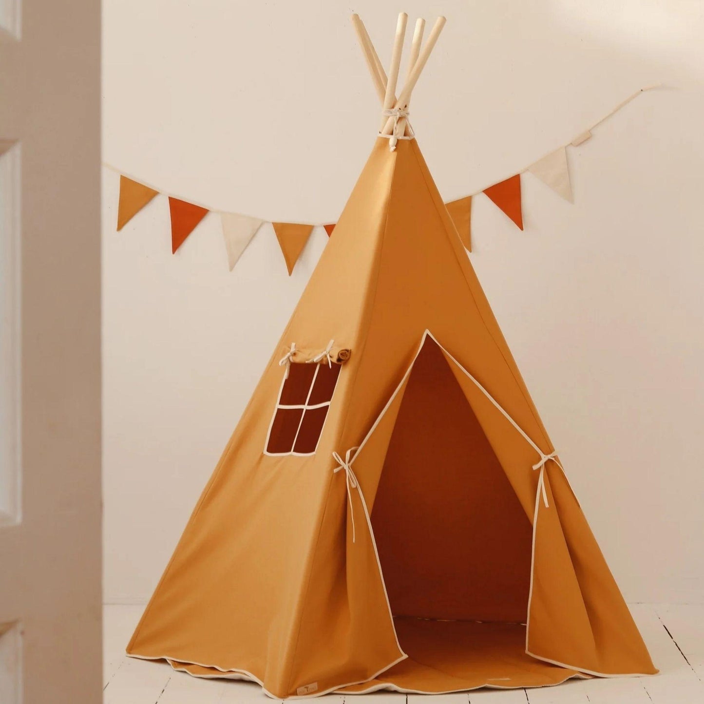 Brown teepee tent with wooden poles against a white wall with small flags.