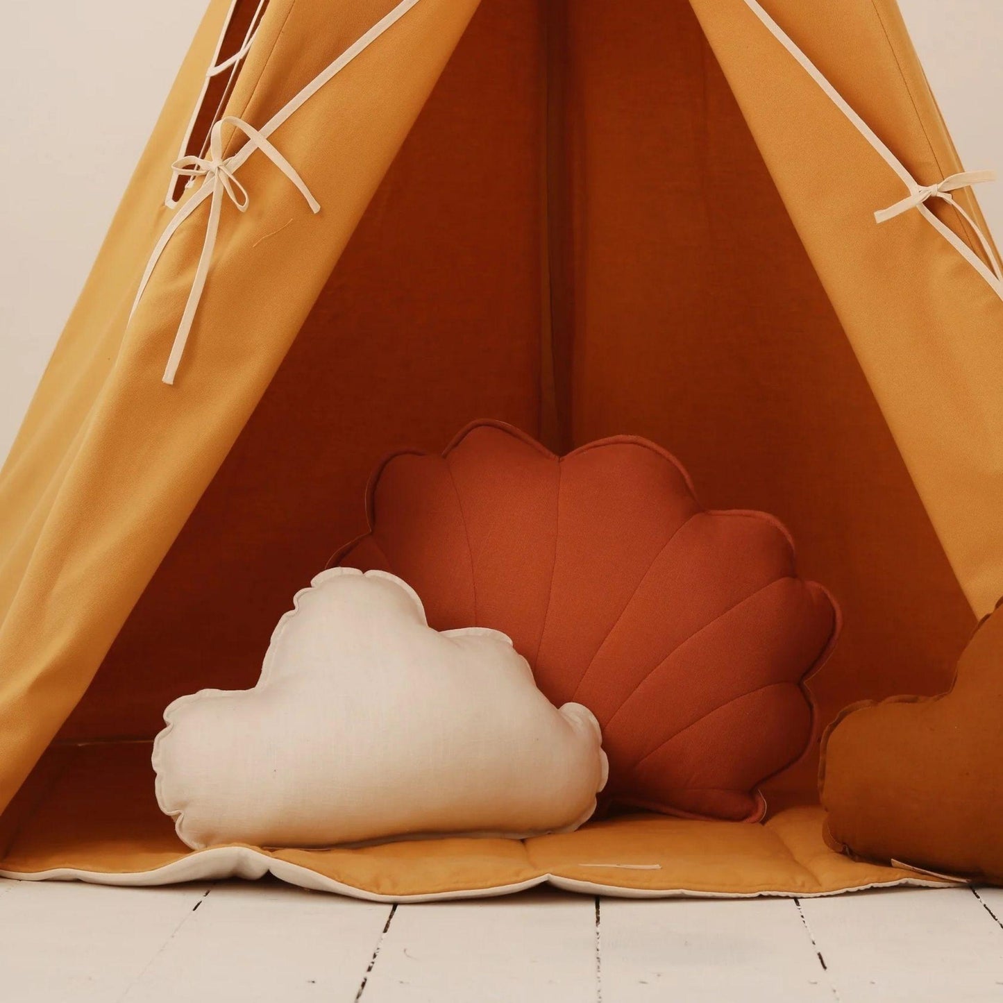 Children's teepee with cloud and shell-shaped cushions on a wooden floor.