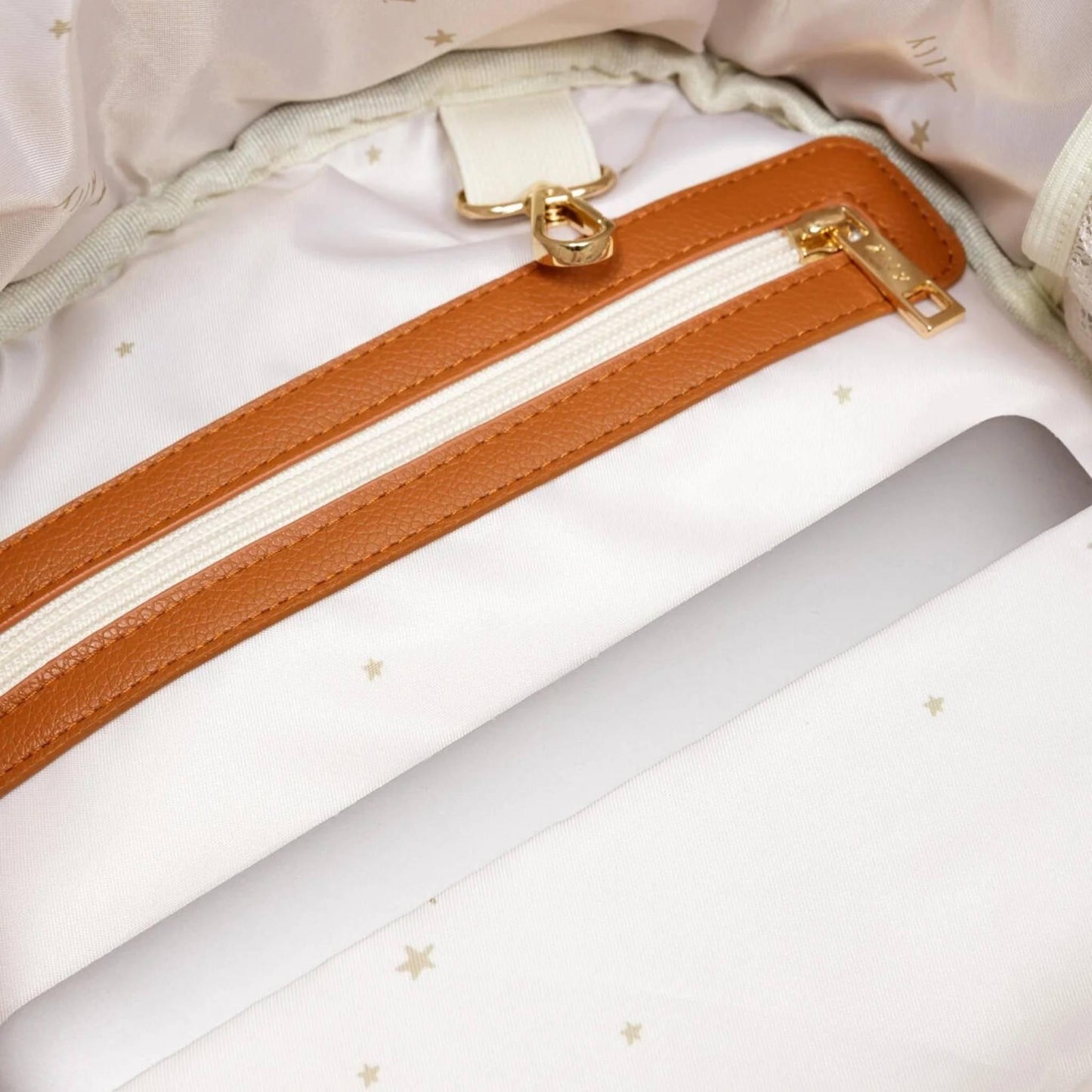 Close-up of a bag with a brown strap and gold zipper on a light background