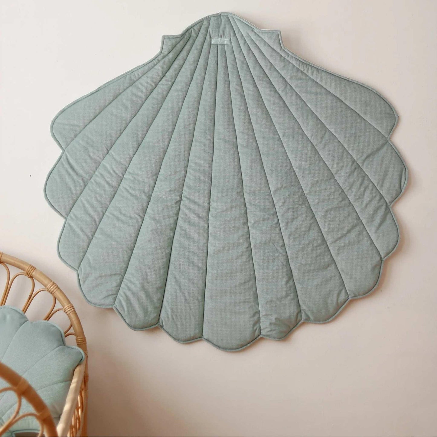 Shell-shaped green rug on a beige wall with a wicker chair and cushion.