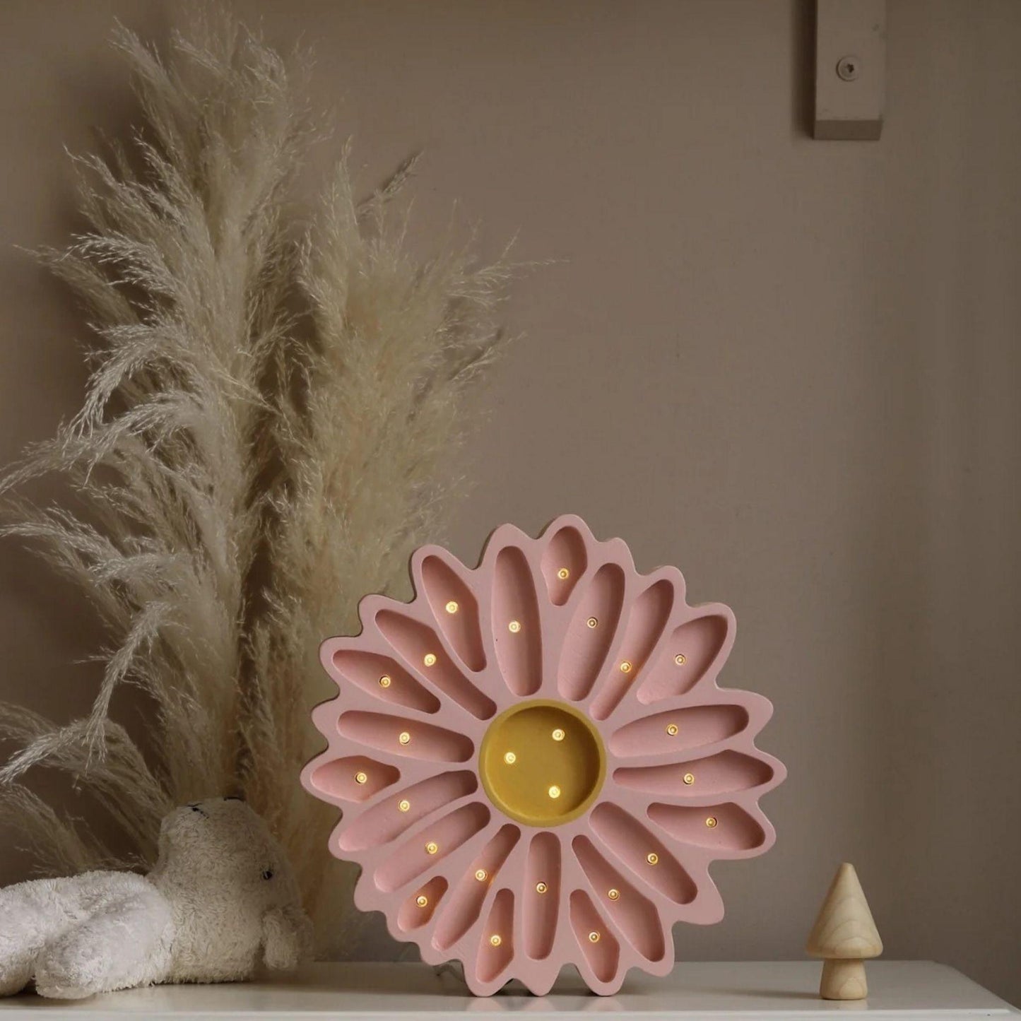 Pink flower-shaped night light on a surface with decorative elements in the background.