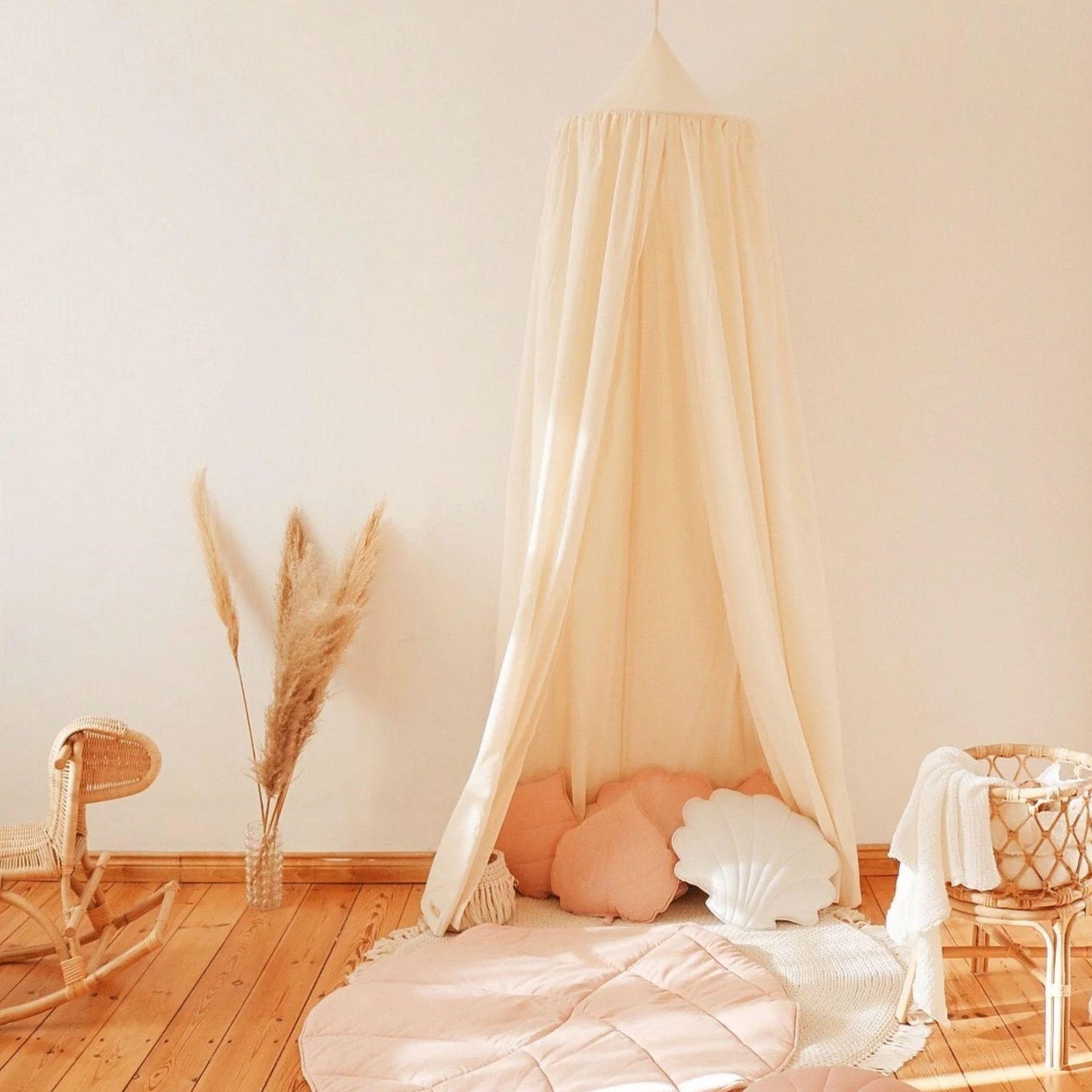 Children's room with a canopy, rocking chair, and decorative pillows on a wooden floor.