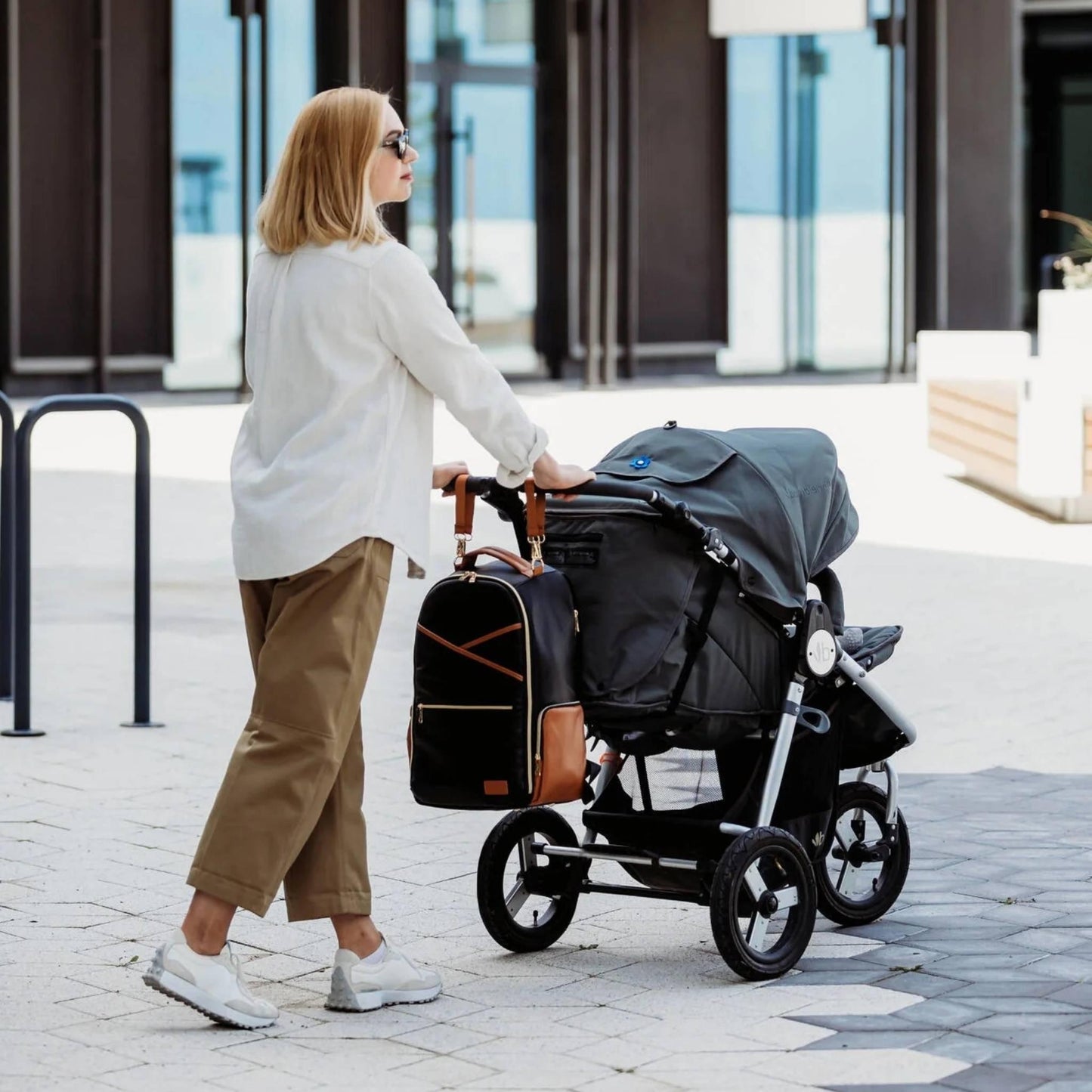 Woman pushing a stroller with a bag attached outdoors.