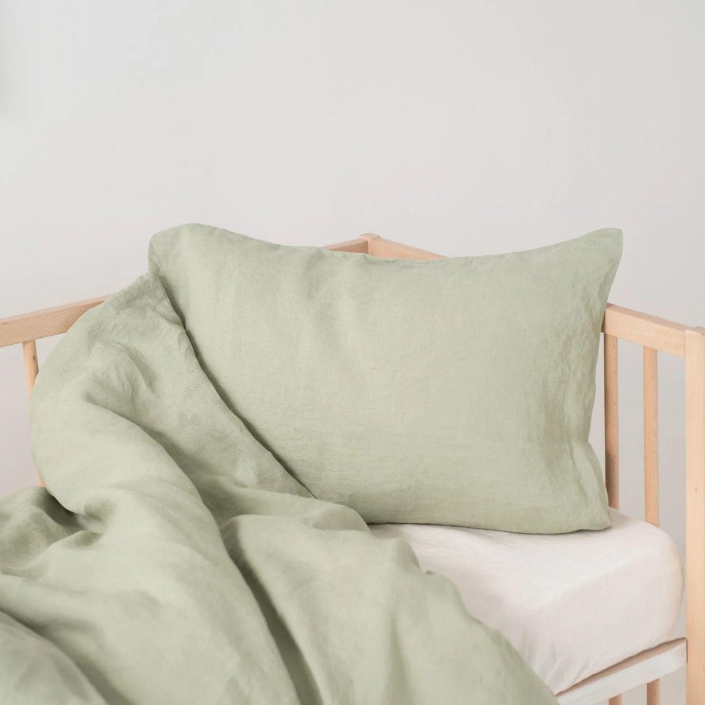Green blanket and pillow on a wooden chair against a white background