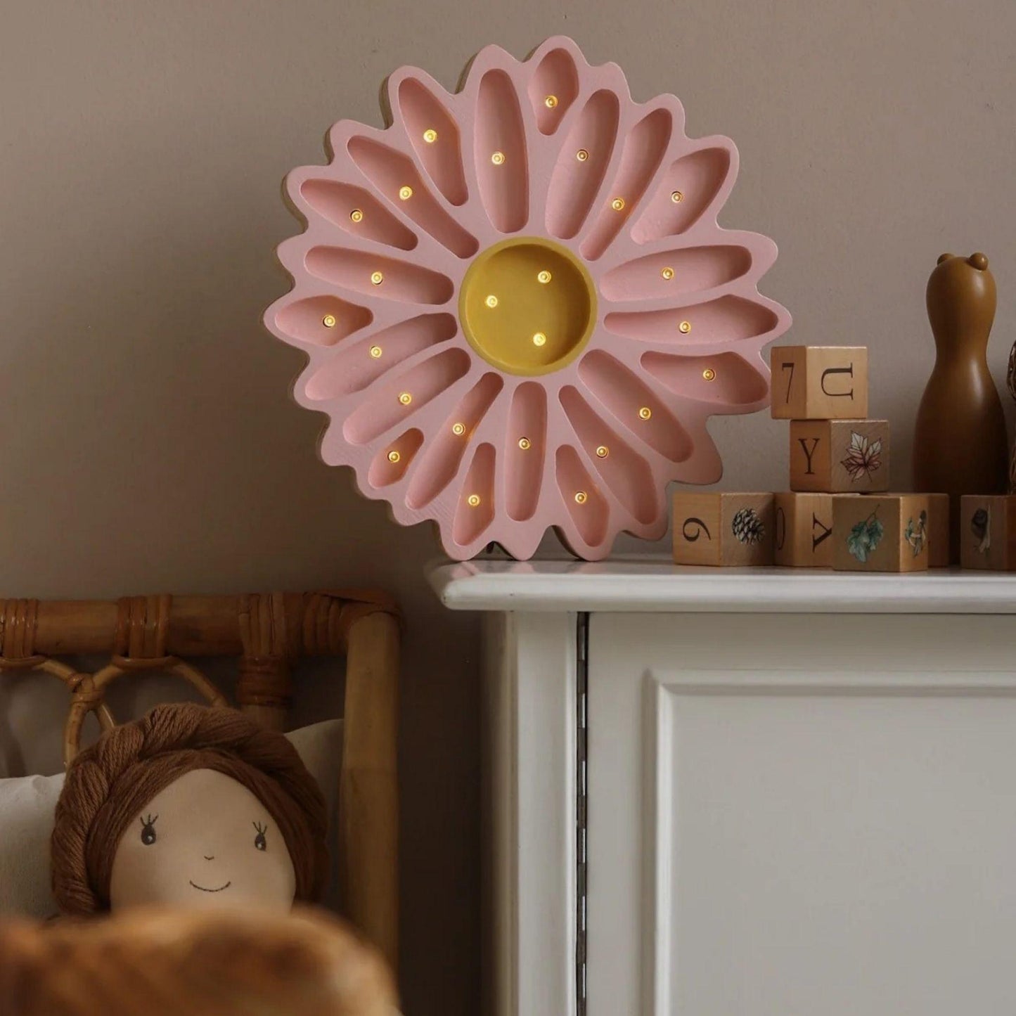 Pink flower-shaped night light on a shelf with wooden blocks and a teddy bear.