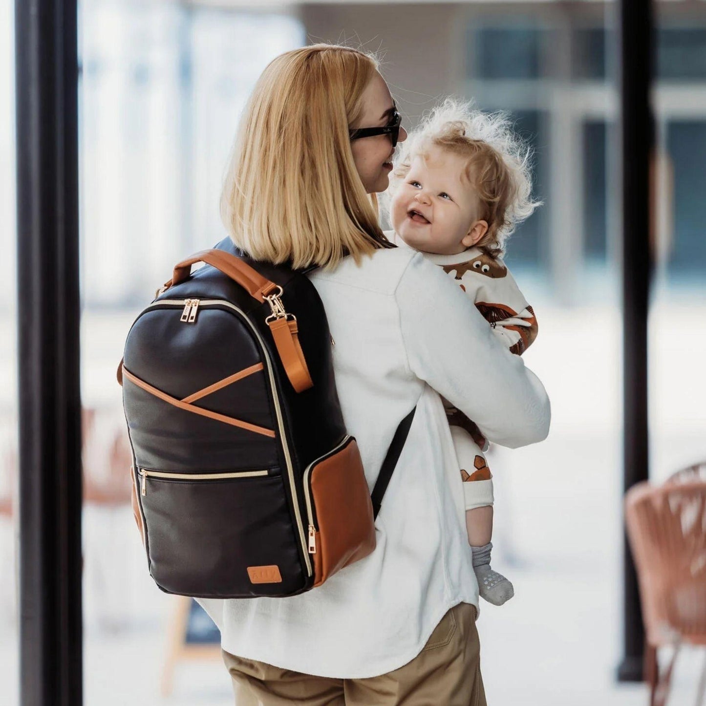 Woman carrying a child and a diaper bag in an indoor setting