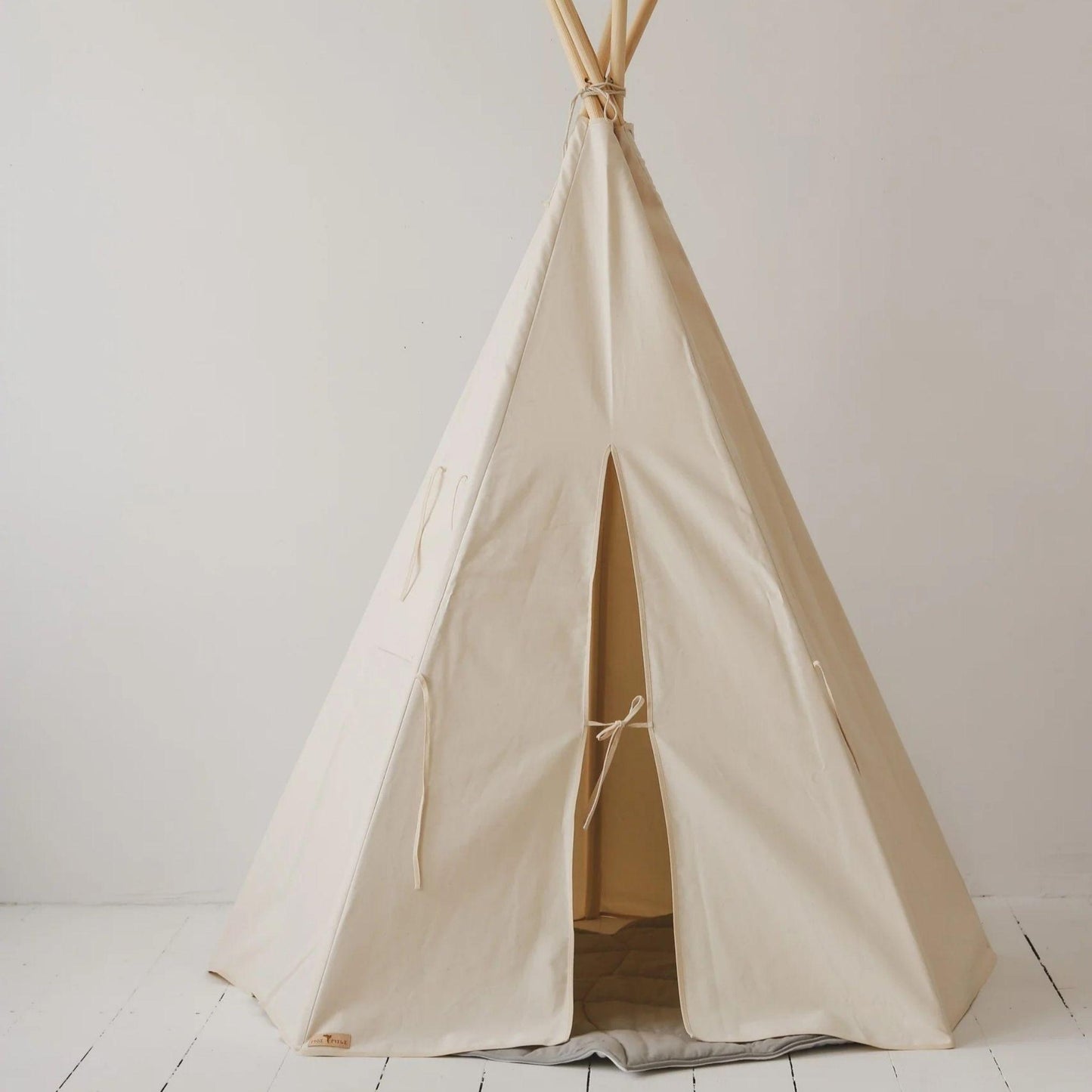 Beige teepee tent on a white floor with a plain white wall background