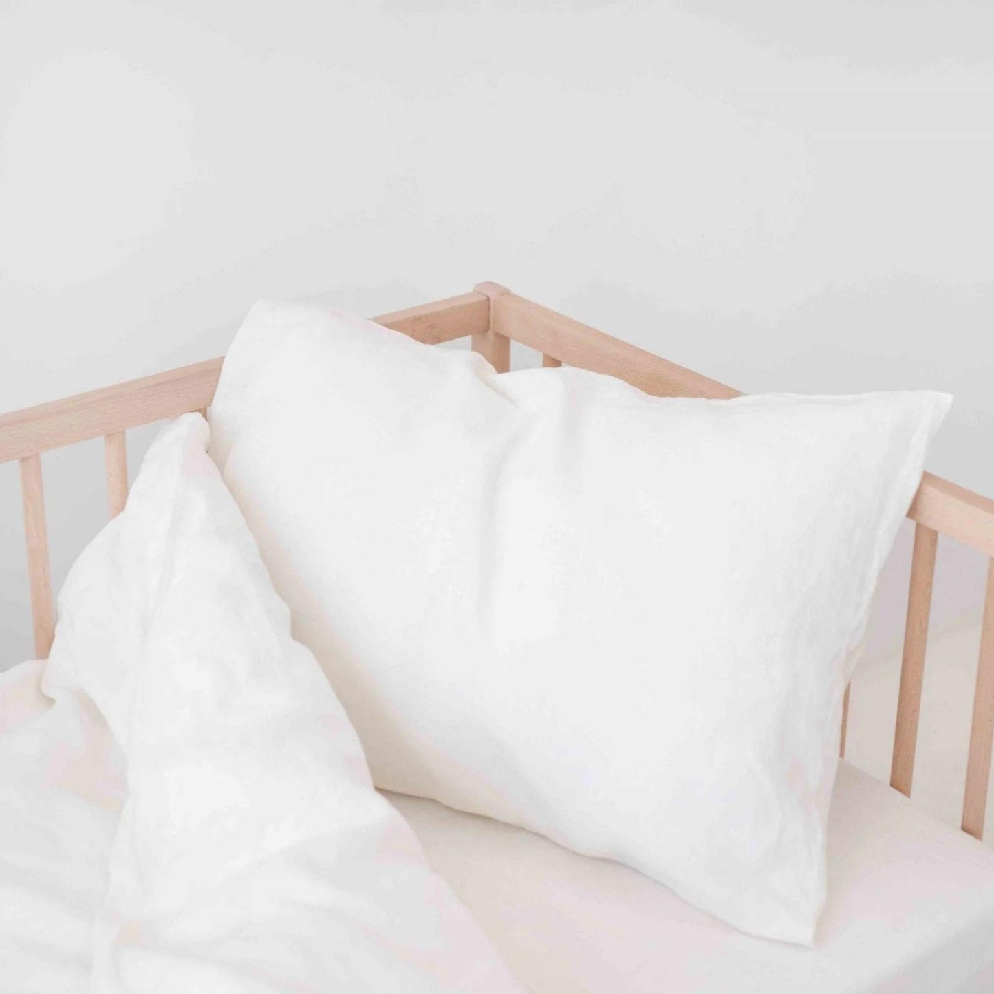 White pillows on a wooden crib against a white wall