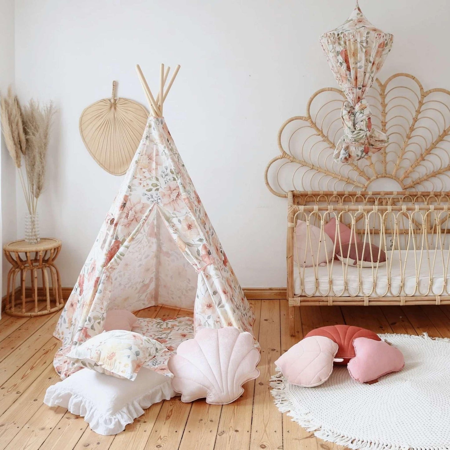 Children's room with a floral teepee, crib, and decorative pillows on a wooden floor.