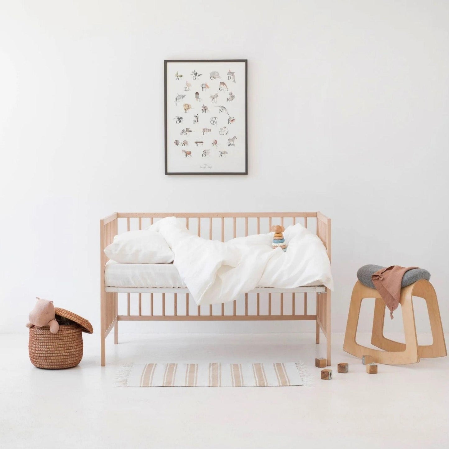 Minimalist bedroom with wooden crib, white bedding, and decorative items on a white background