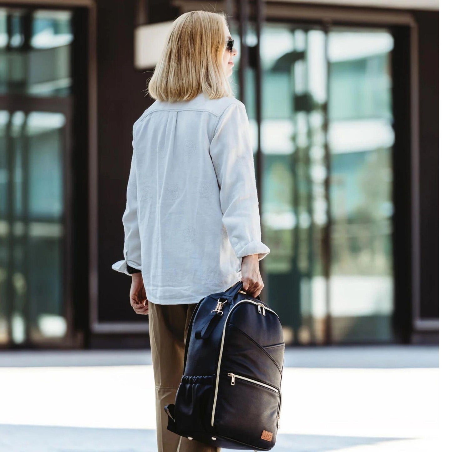 Person holding a black backpack in front of a modern building