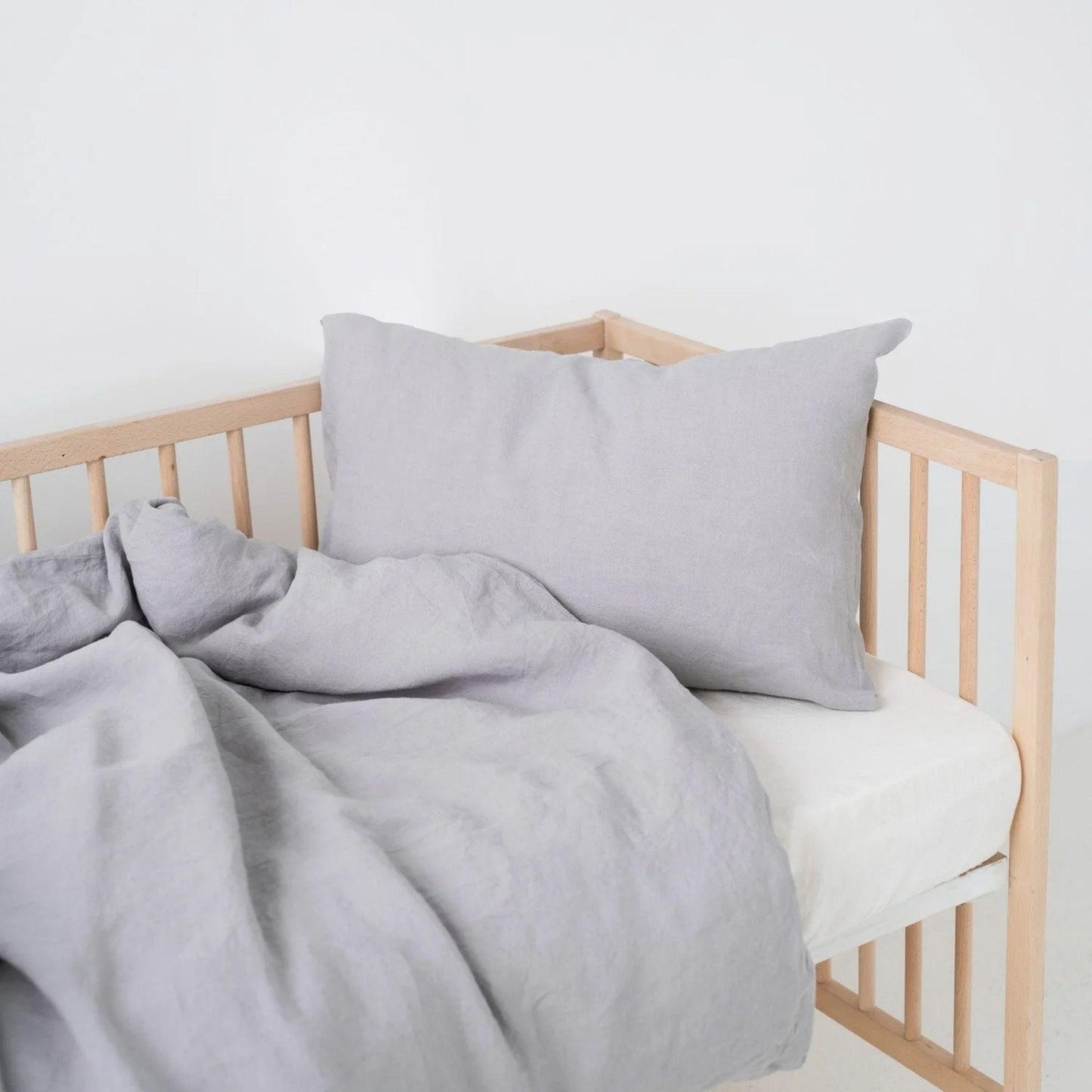 Gray bedding set on a wooden crib with a white background