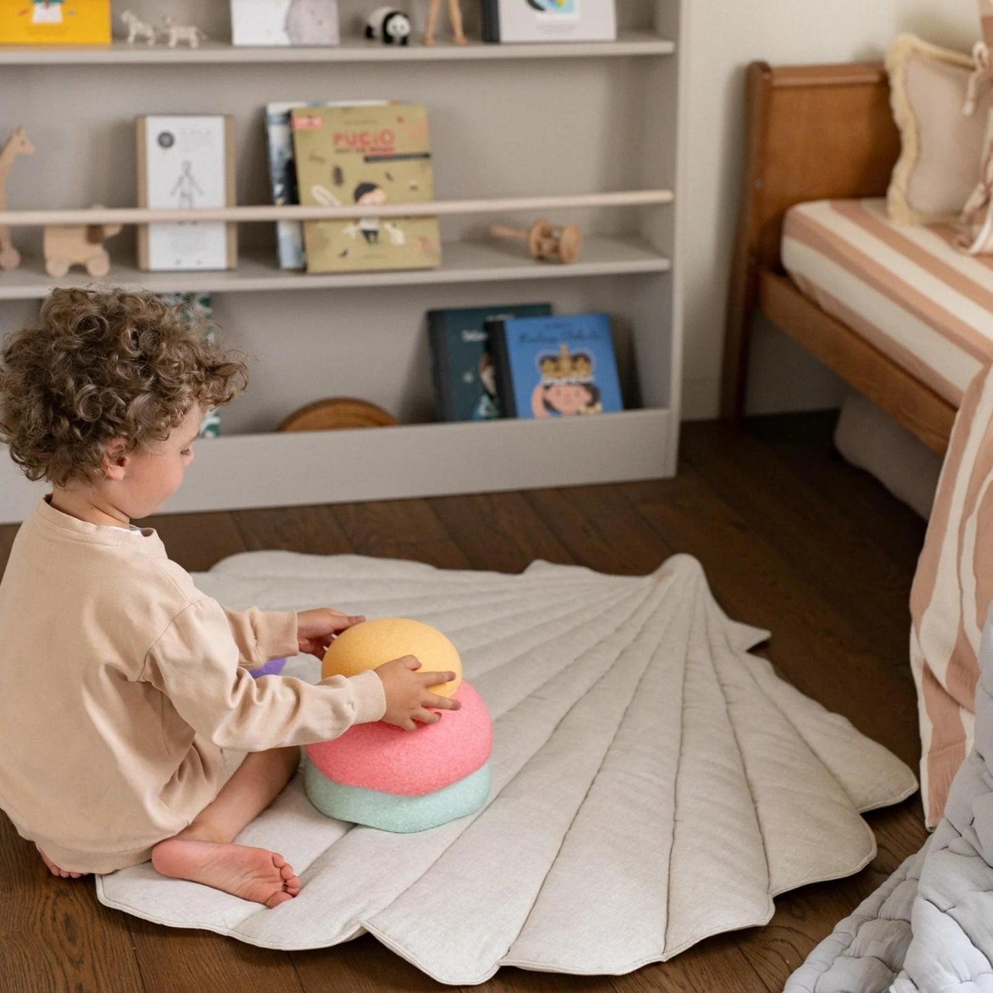 Child playing with colorful toys on a white blanket in a room with shelves and furniture.