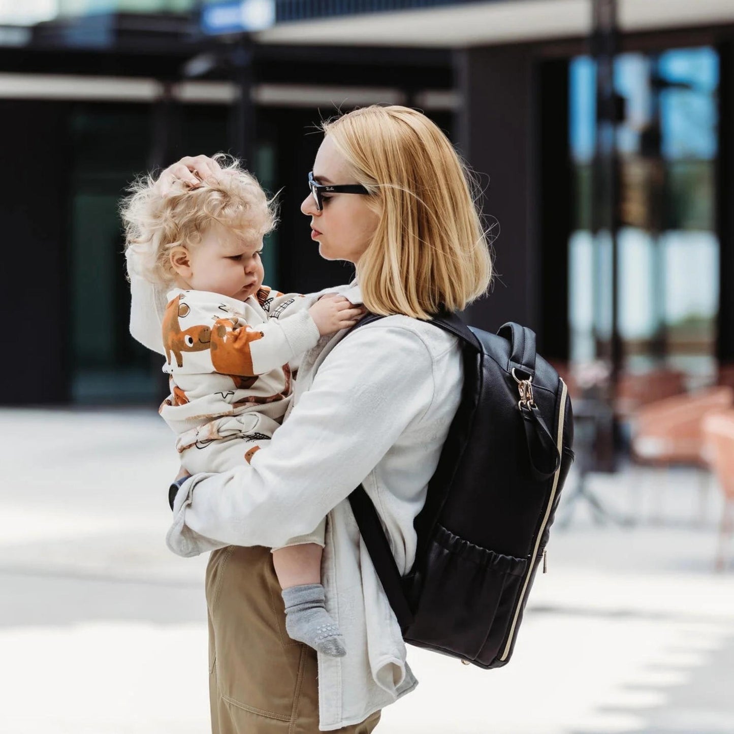 Woman holding a child with a backpack in an urban setting