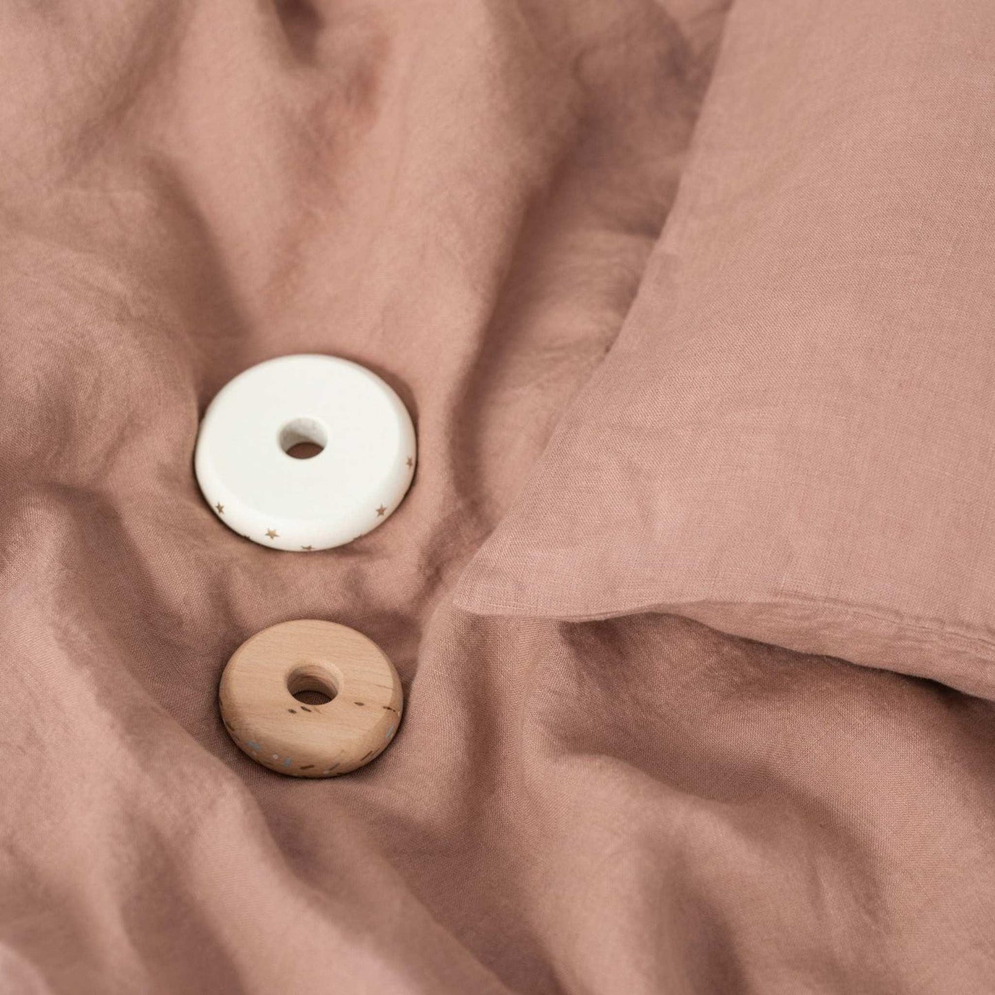 Two ceramic donut-shaped objects on a soft pink fabric surface.