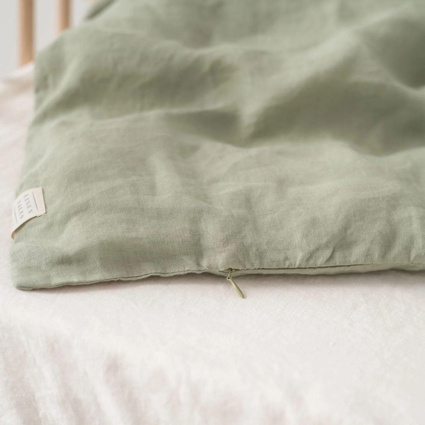 Green pillow on a bed with a visible brand label.