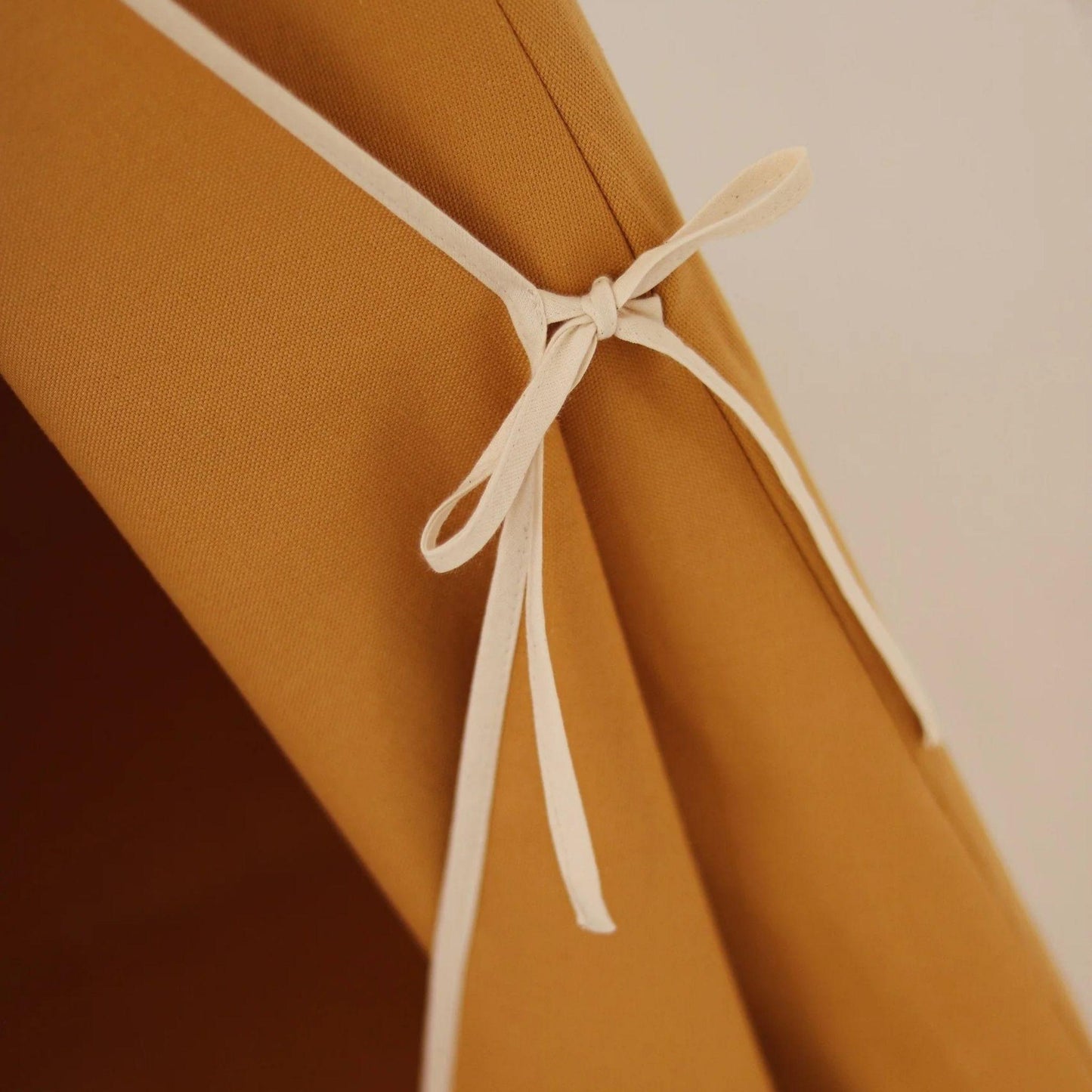 Close-up of a mustard yellow fabric with a white ribbon tied around it against a neutral background.
