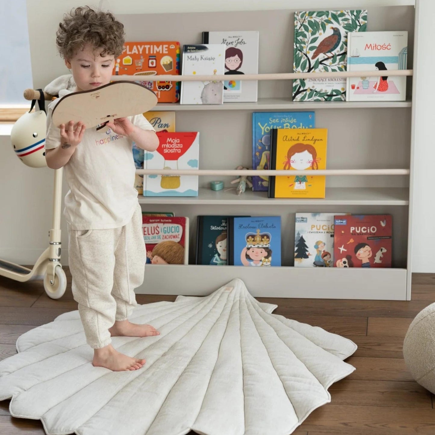 Child playing with a wooden toy in front of a bookshelf filled with books