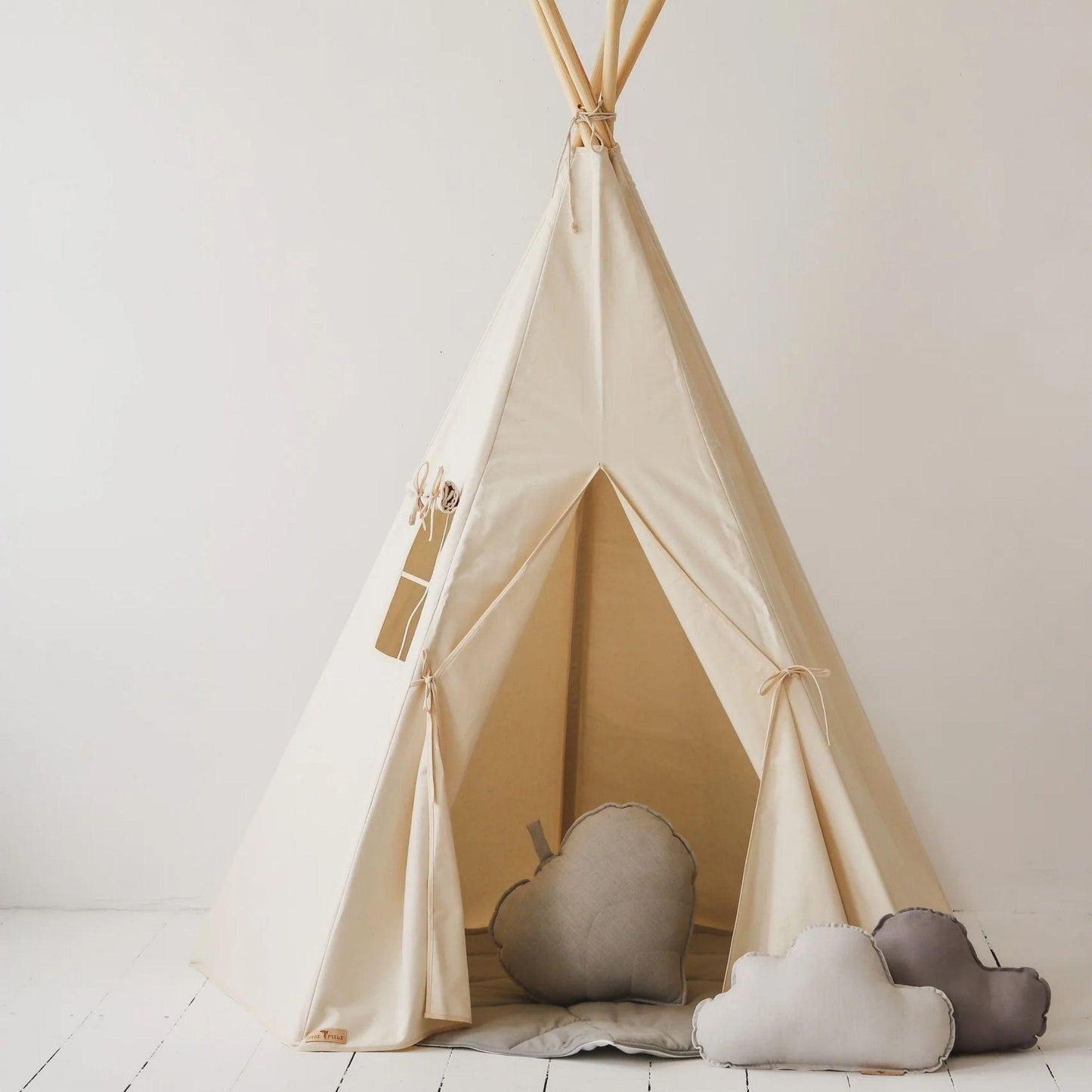 Beige children's teepee with soft pillows on a white floor and wall