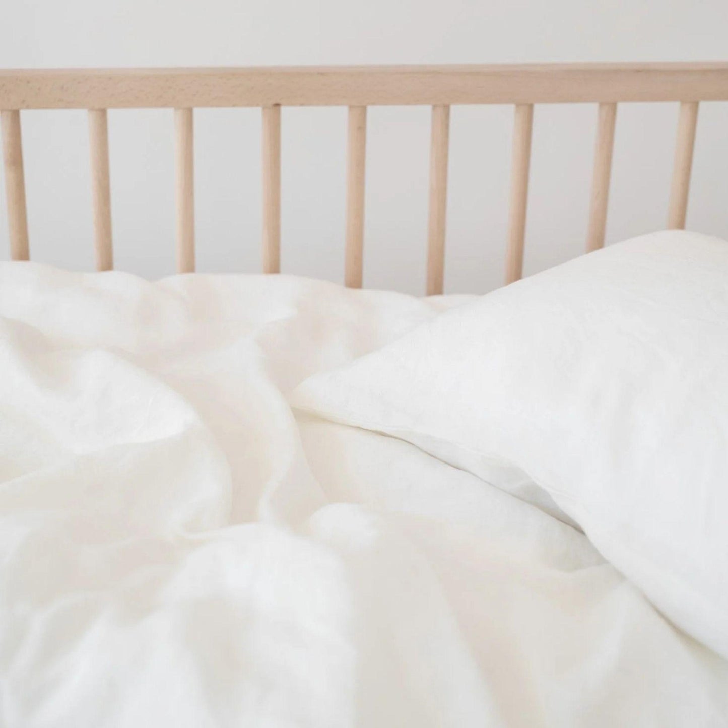 Bed with white bedding and a wooden headboard against a plain wall
