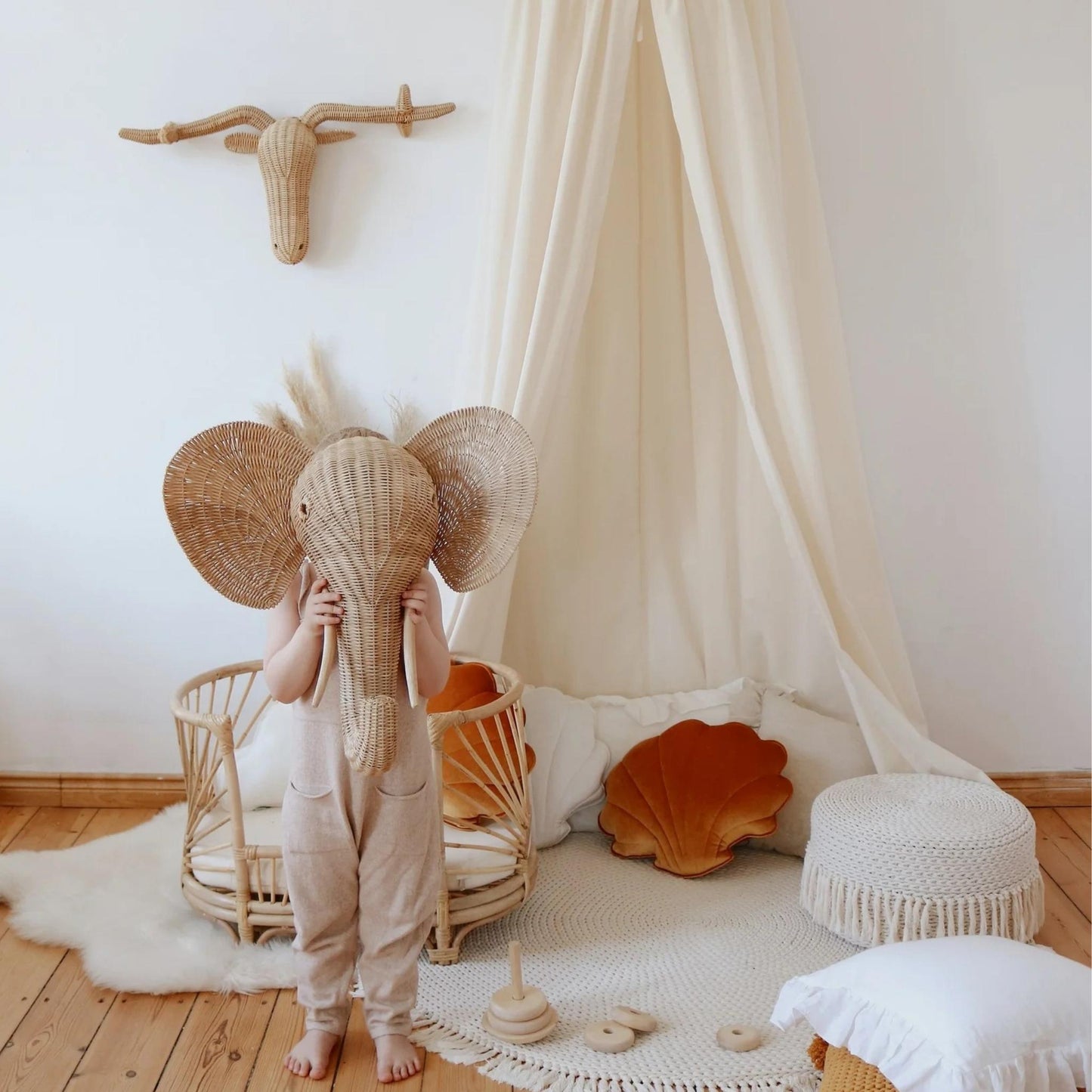 Child wearing a woven elephant costume in a cozy room with white walls and wooden floor.
