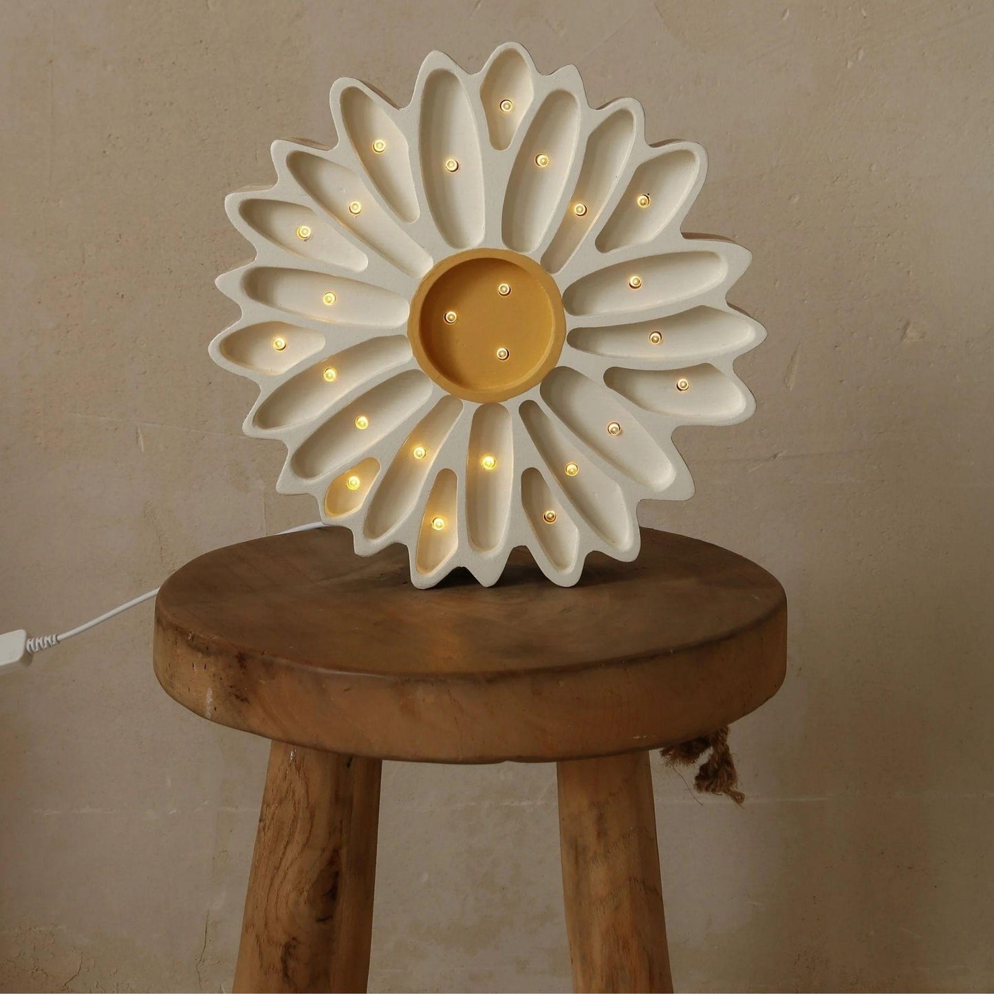 Decorative lamp shaped like a flower on a wooden stool against a beige wall.
