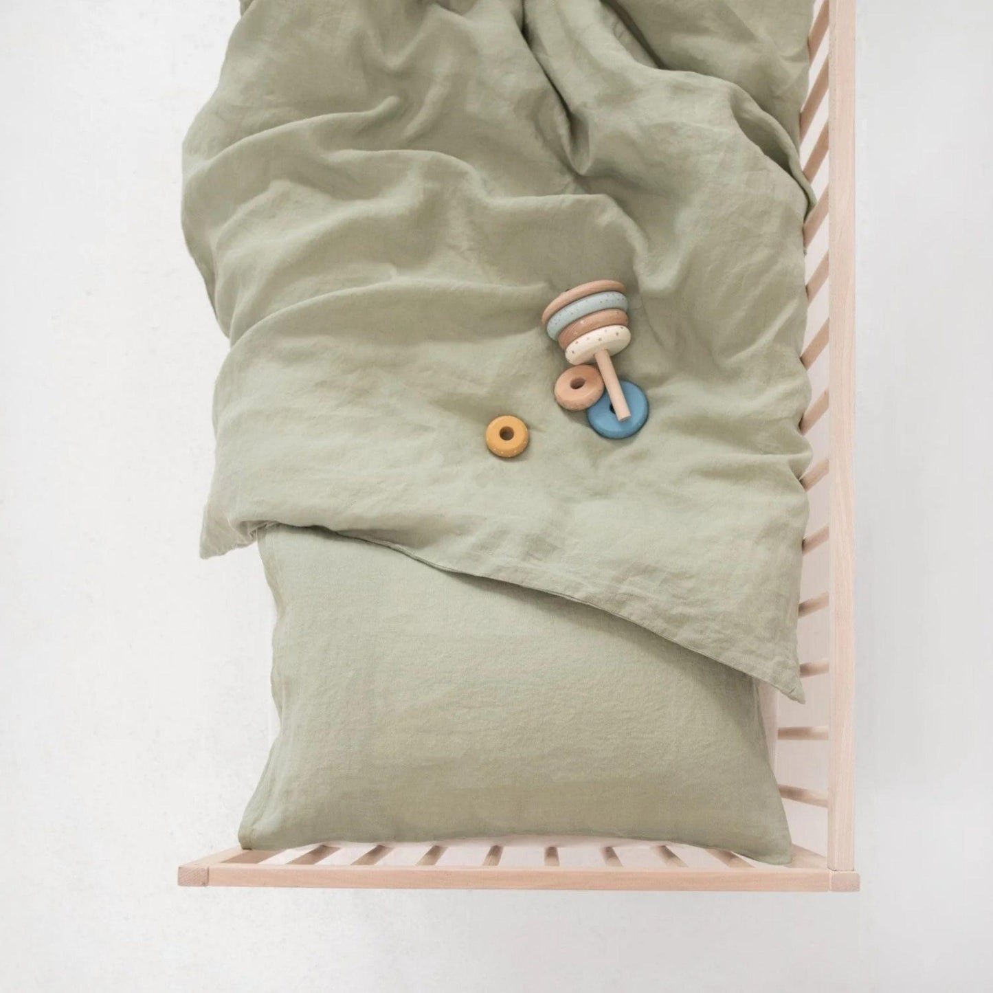 Green baby blanket with a toy on a wooden crib against a white background