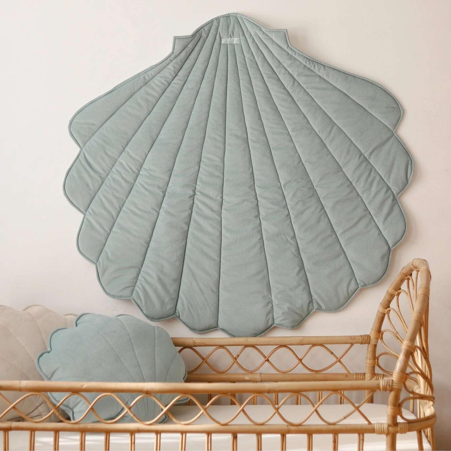 Shell-shaped green cushion on a wall above a rattan crib