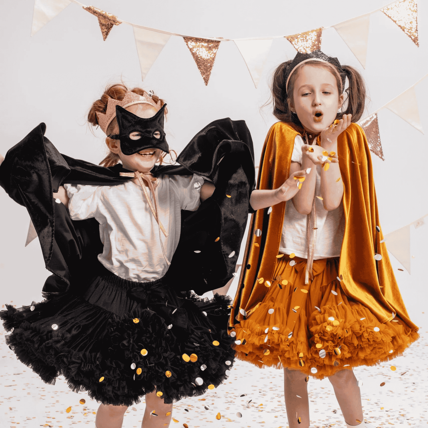 Two children in superhero costumes with black and orange capes, standing against a light background.