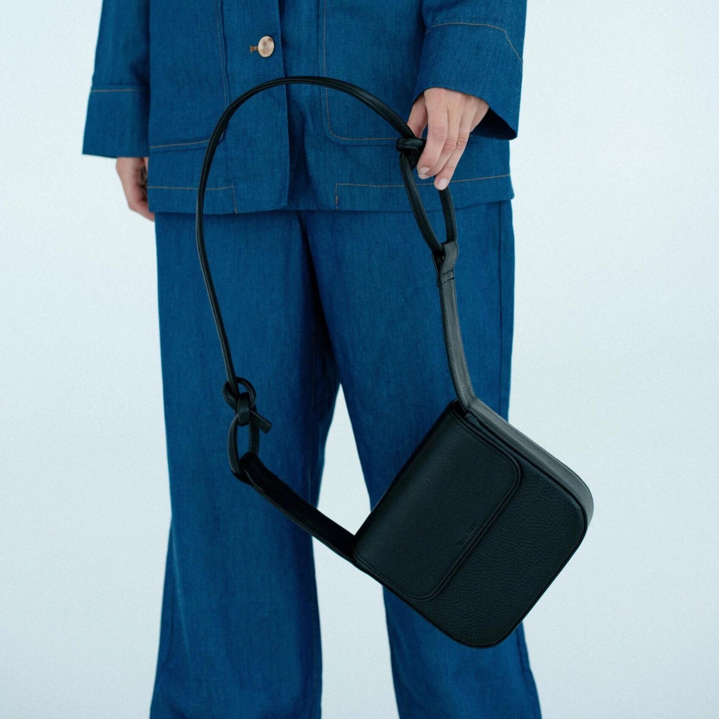 Person wearing a blue outfit holding a black crossbody bag against a light blue background