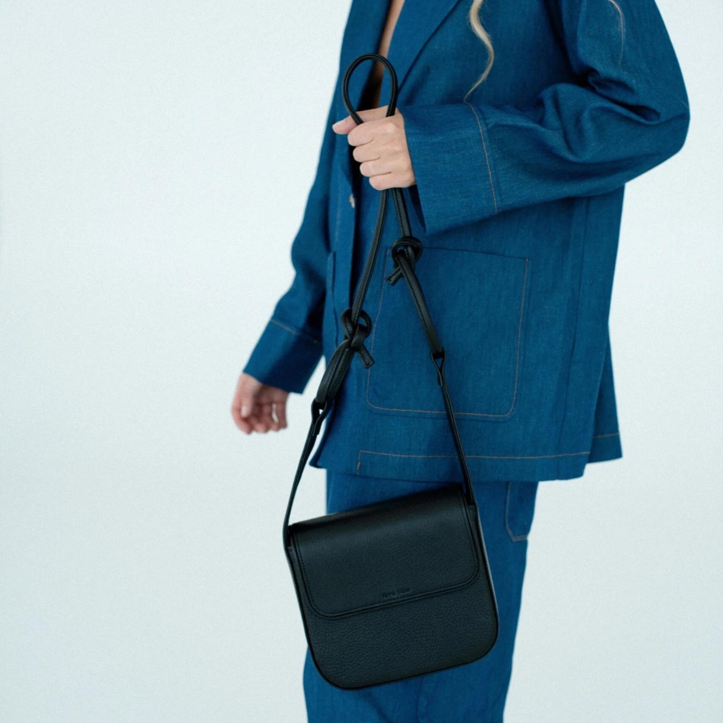 Person wearing a blue suit holding a black handbag against a light background