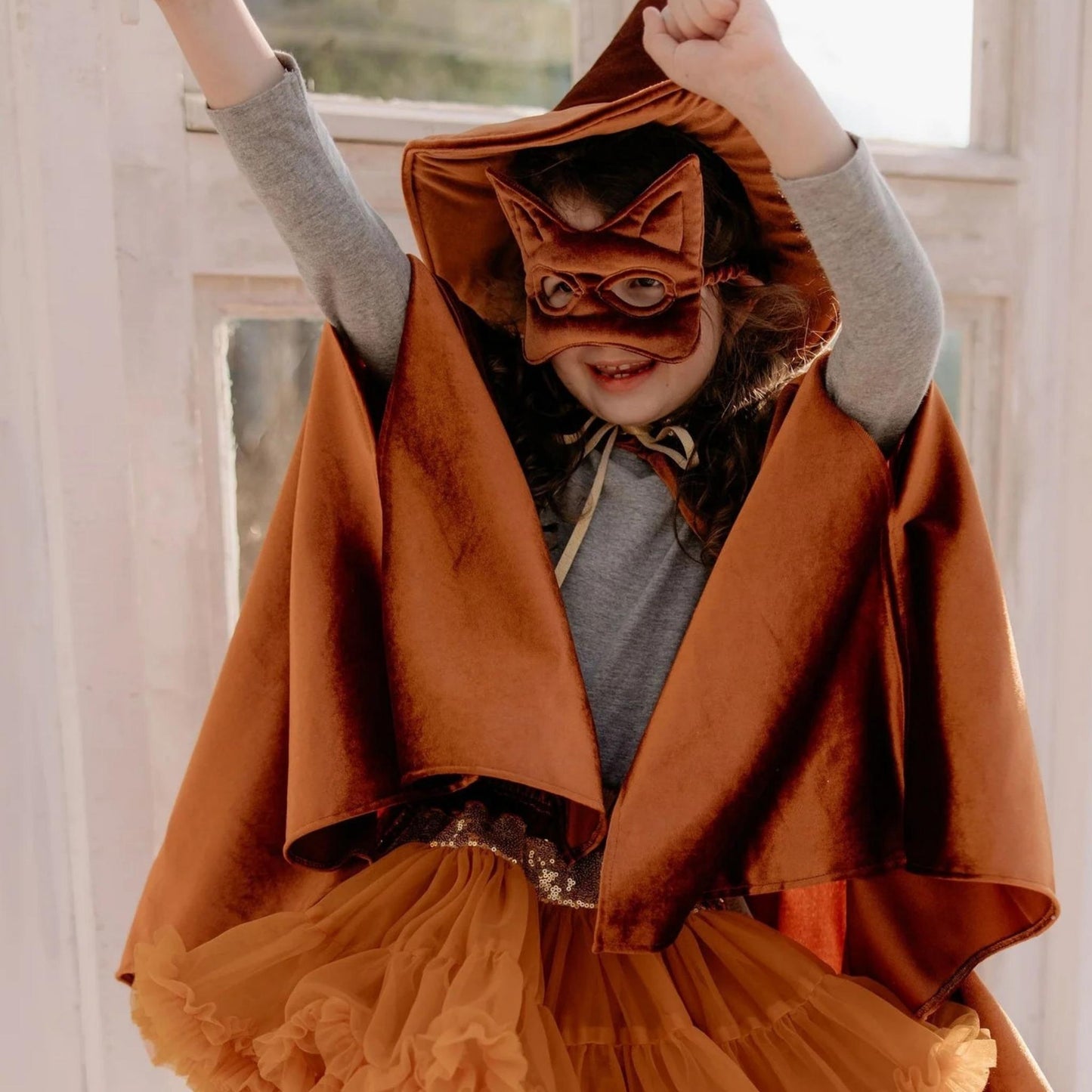Child wearing a brown hooded cloak and mask indoors