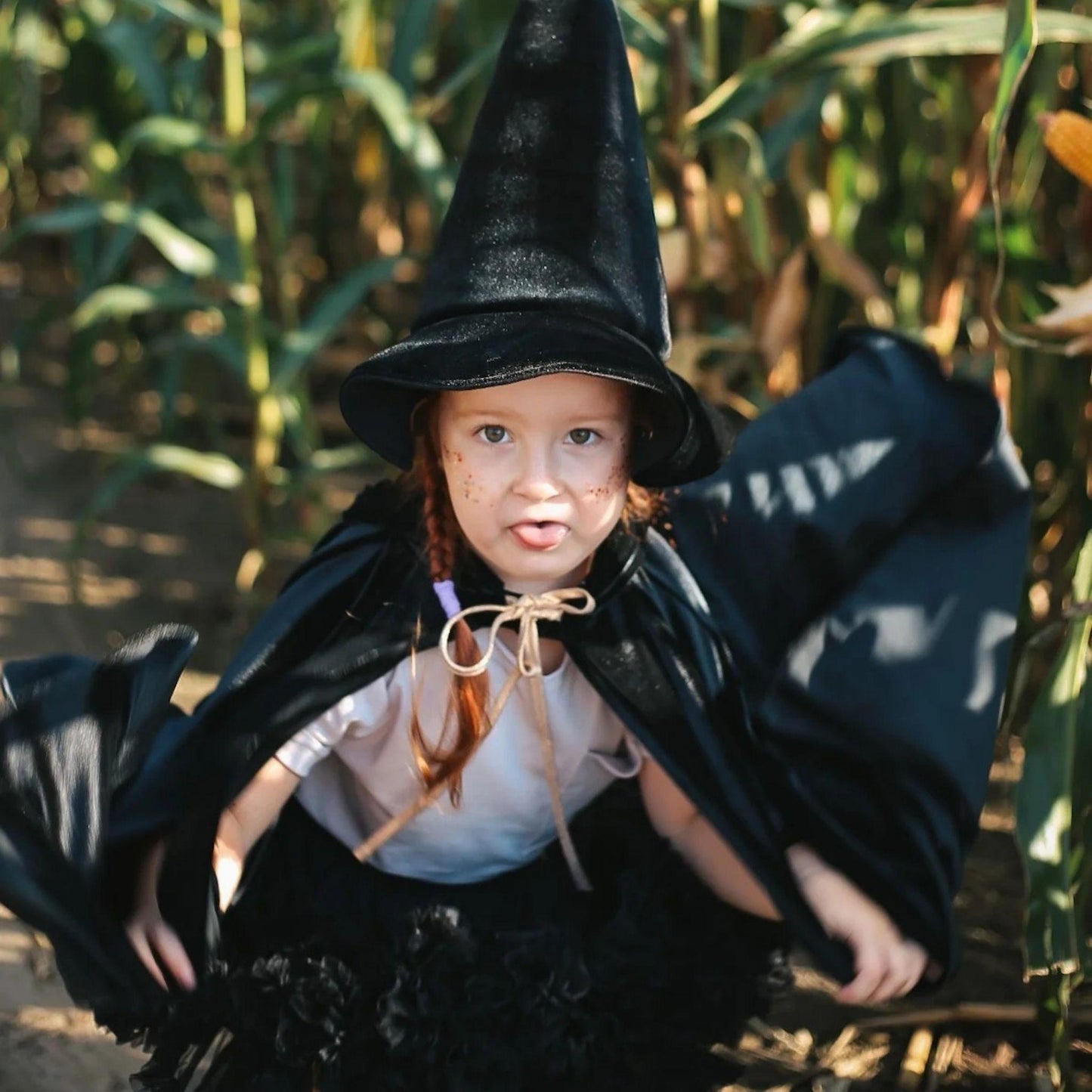 Child in a witch costume standing in a cornfield
