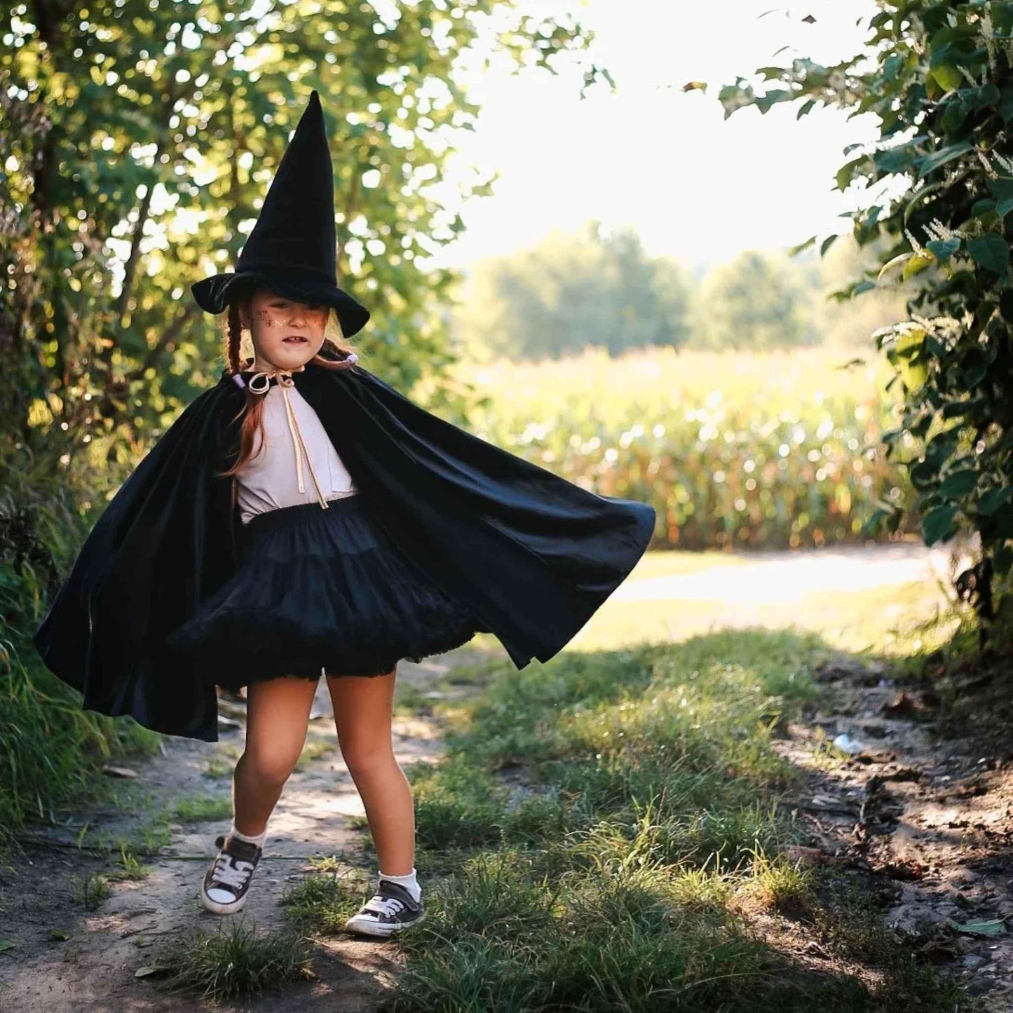 Child in a witch costume standing outdoors on a sunny day