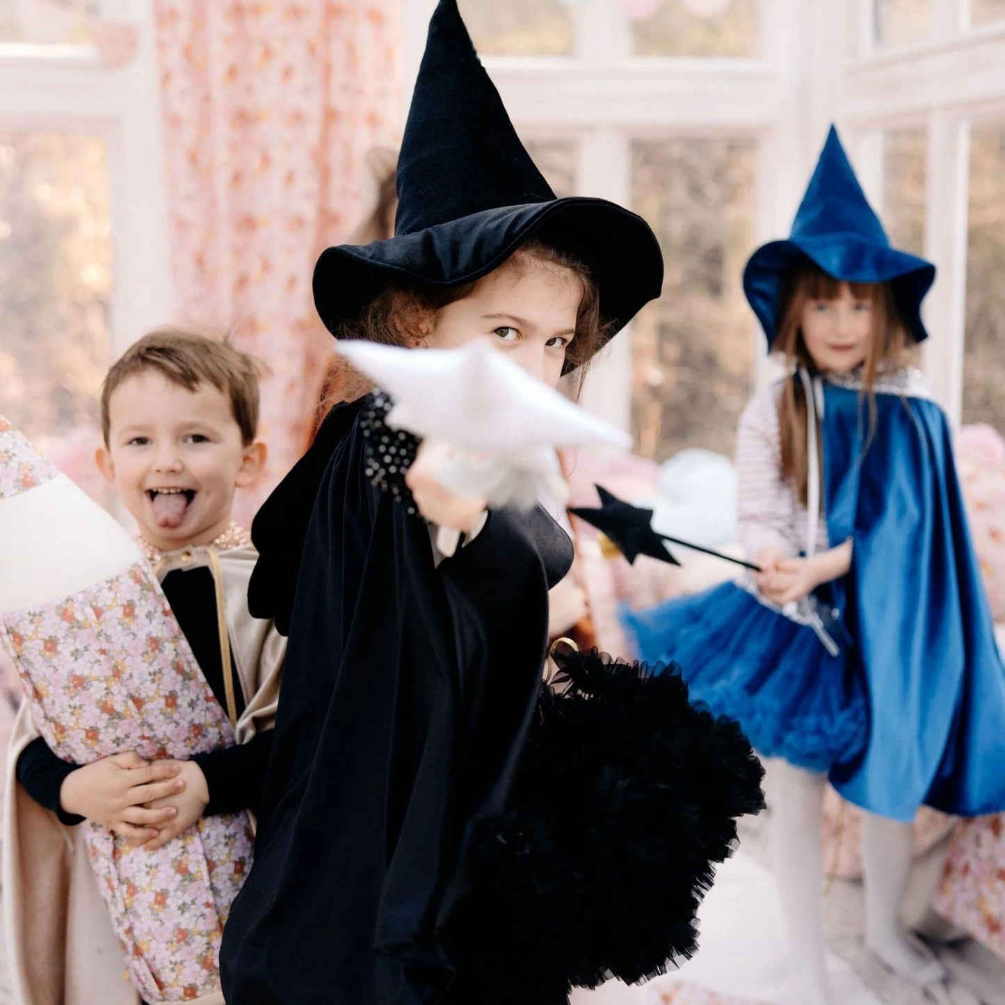 Children in Halloween costumes, including a witch and a wizard, with a decorative indoor background.
