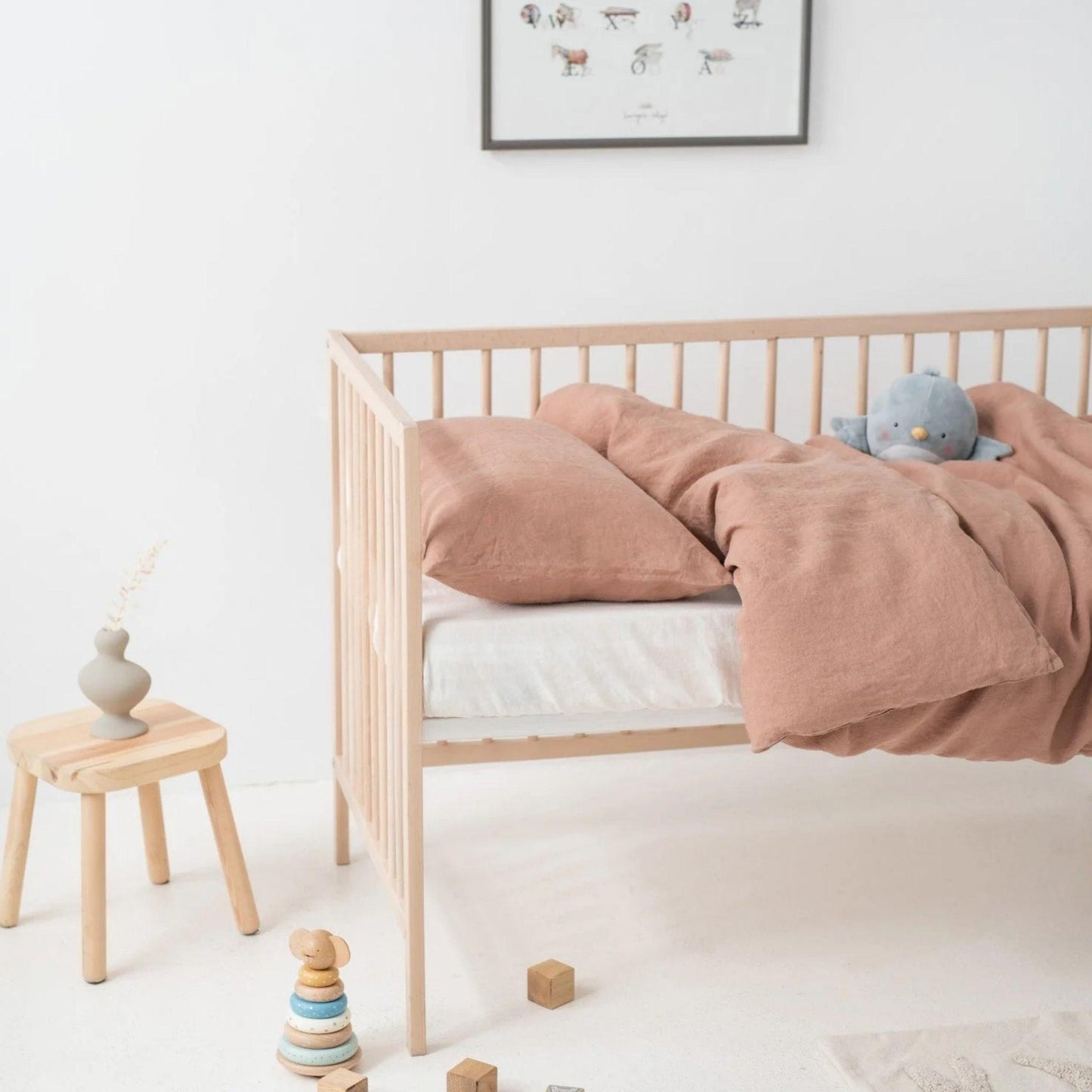 Nursery room with a wooden crib, pink bedding, and toys on a white floor.