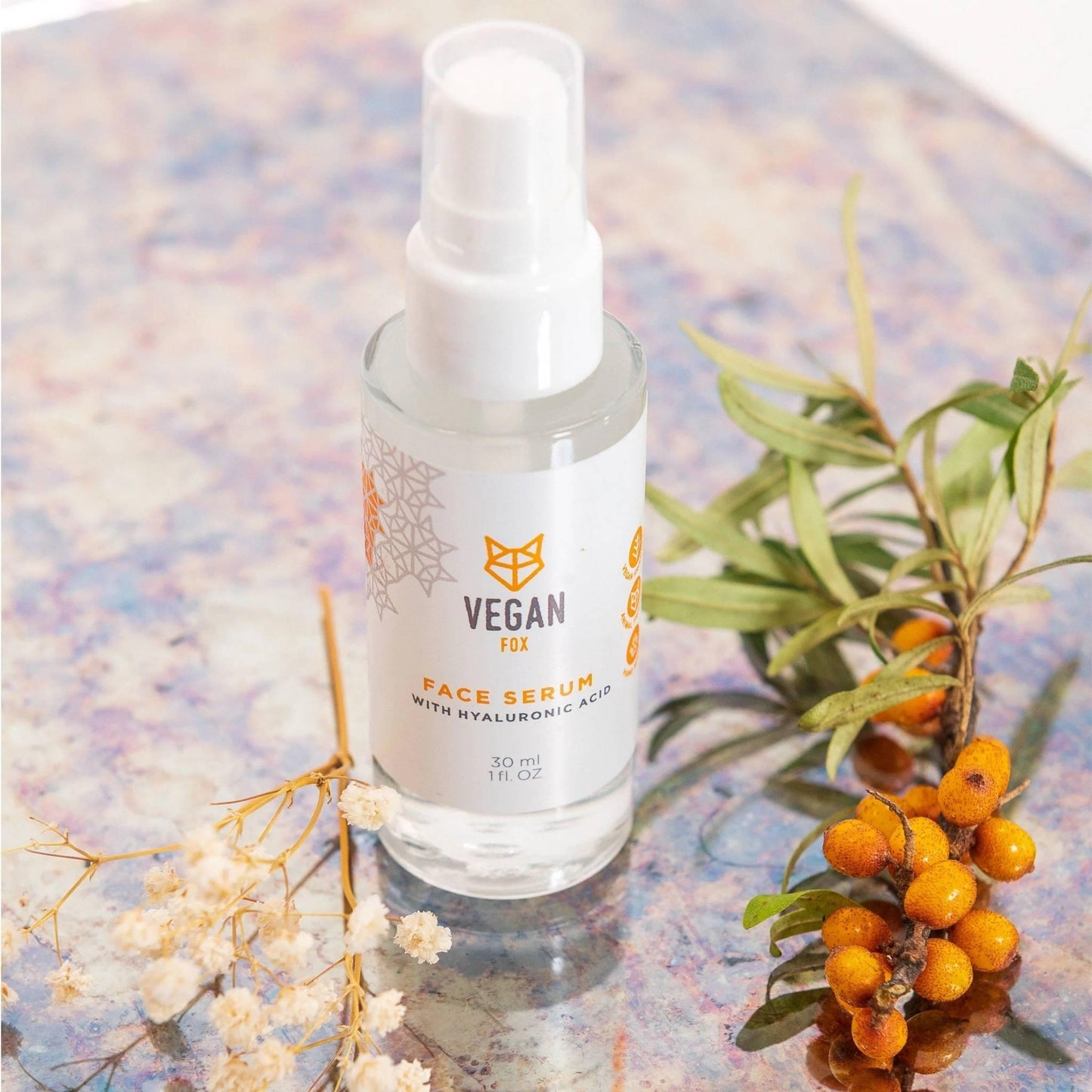 Face serum bottle with vegan label on a decorative background with plants and berries