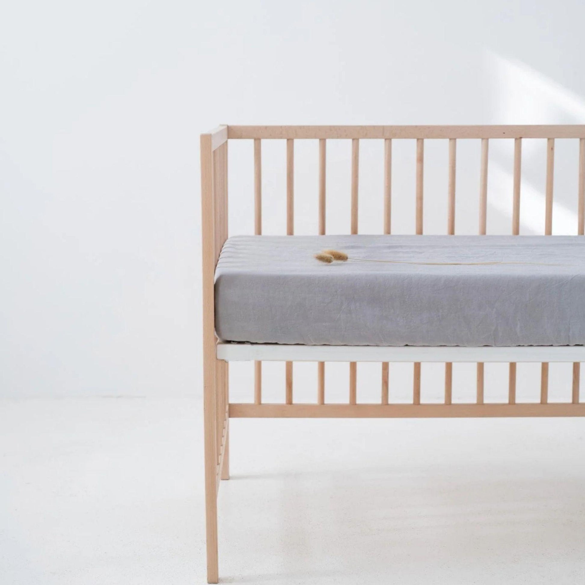 Wooden crib with a gray mattress on a white background