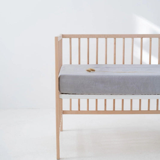 Wooden crib with a gray mattress on a white background