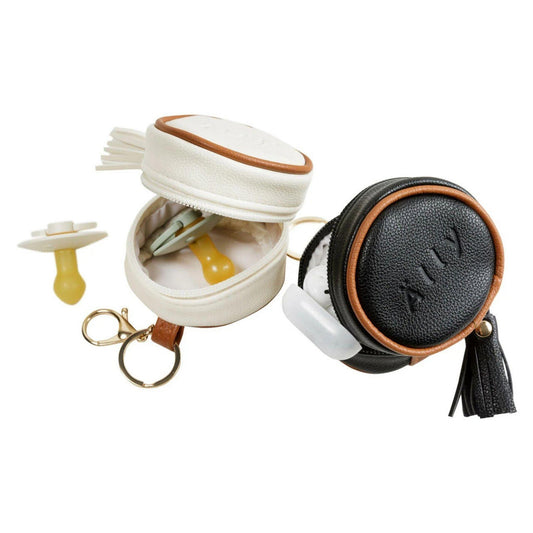 Black and brown circular pouch with tassel, white container with beige lid, and yellow pacifier on a white background