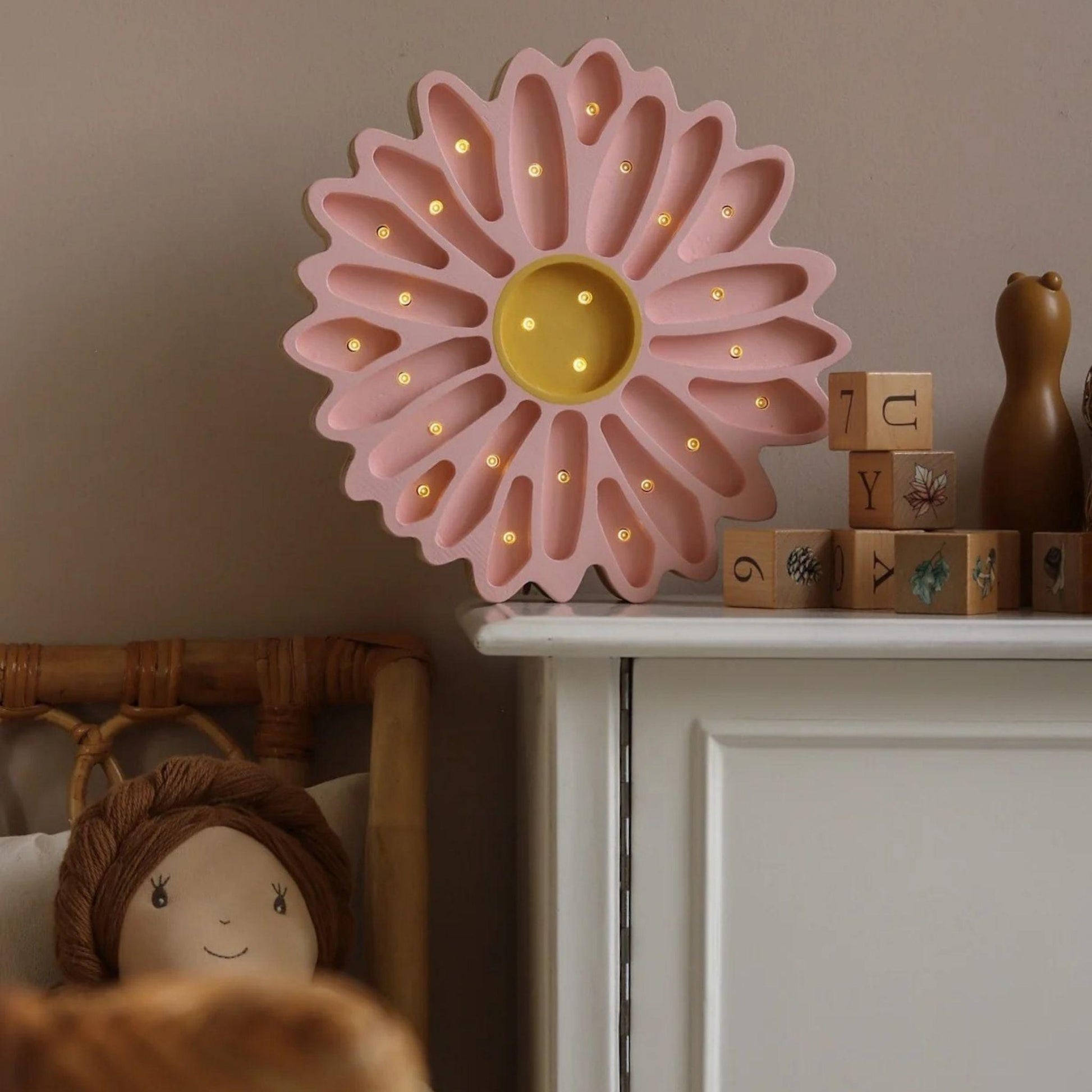 Pink flower-shaped night light on a shelf with wooden blocks and a teddy bear.