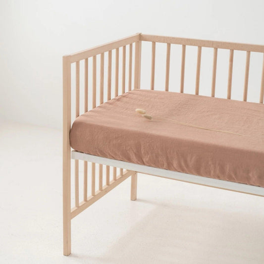 Wooden crib with a beige mattress on a white background