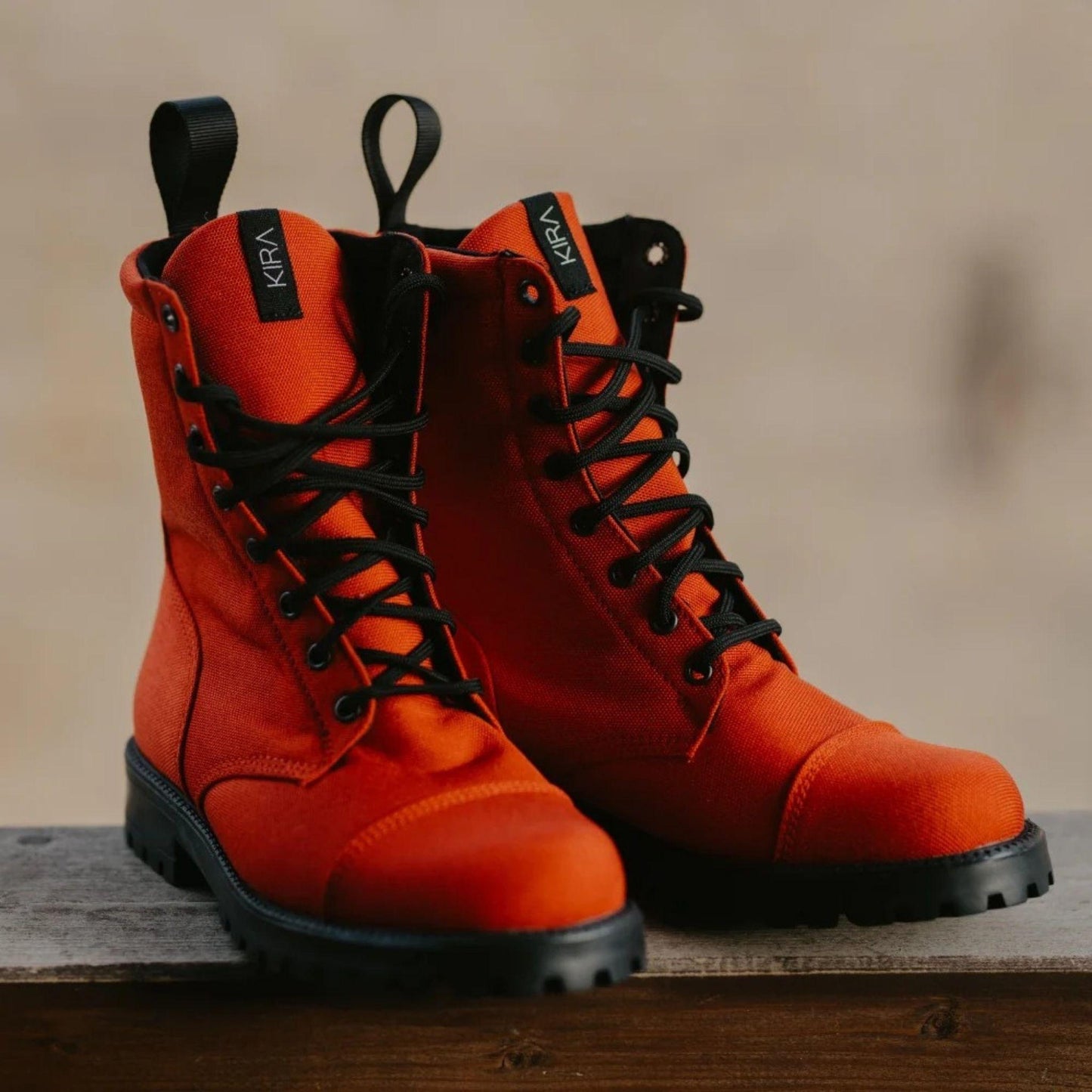 Pair of orange boots with black laces on a wooden surface