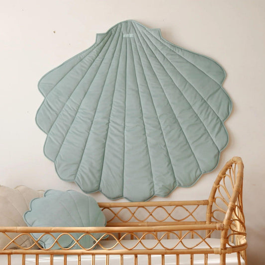 Shell-shaped green cushion on a wall above a wicker crib