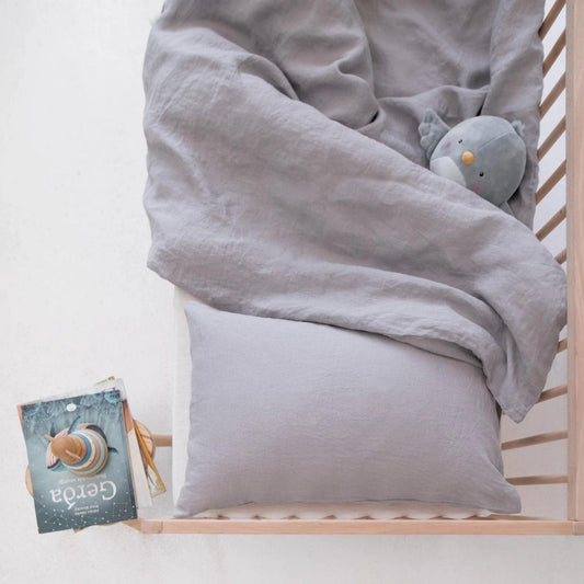 Gray crib set with a pillow and stuffed animal in a crib, featuring a book on a white background.