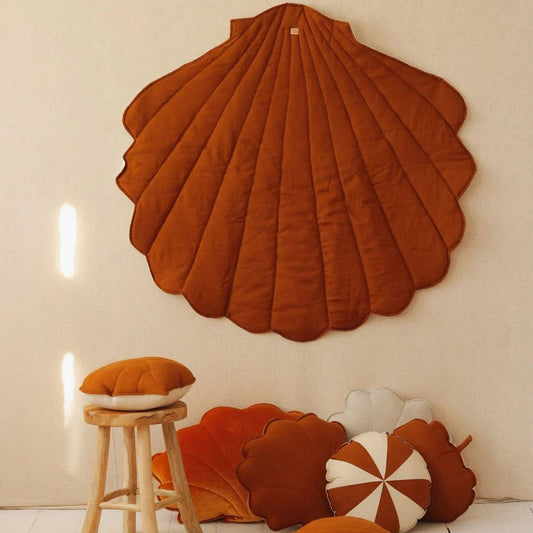 Shell-shaped brown cushion on a wall with smaller cushions on the floor and a stool.