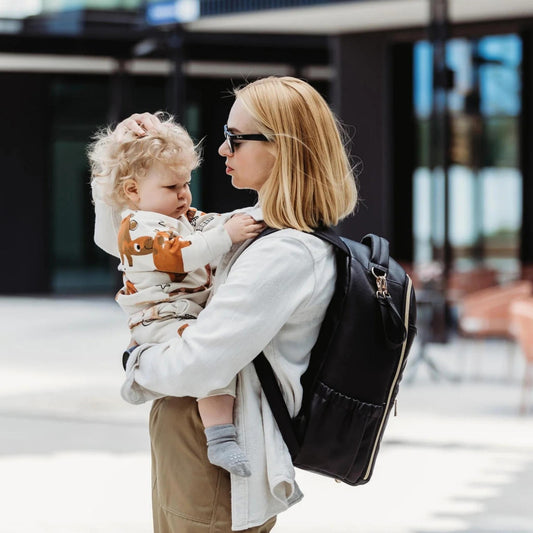 Woman holding a child with a backpack in an urban setting