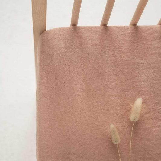 Close-up of a wooden chair with a  beige linen sheet and two dried plants on a white background