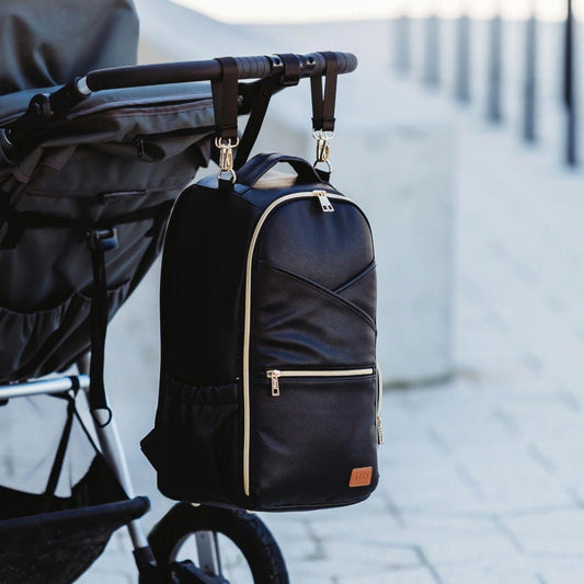 Black backpack with gold accents attached to a stroller on a blurred background